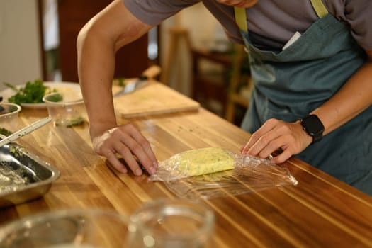 Close up of hands wrapping freshly made compound butter on a wooden countertop.