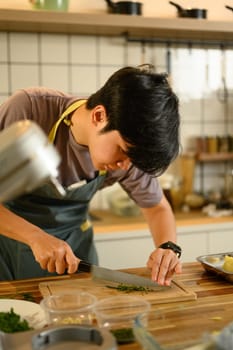 Focused man chopping fresh herbs on a wooden cutting board for compound butter.