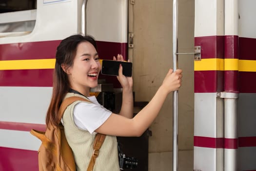 Eagerly ready for her adventure, a young woman smiles as she holds her phone at the train door, embodying travel enthusiasm.