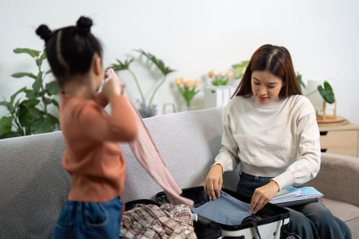 A young girl enthusiastically helps her mother pack by selecting clothes and sharing her thoughts on what to bring for their family trip.