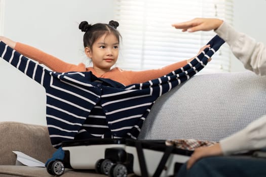 The cheerful moment captures a young girl playfully trying on a sweater during packing time, reflecting the joy and excitement of preparing for a family vacation.