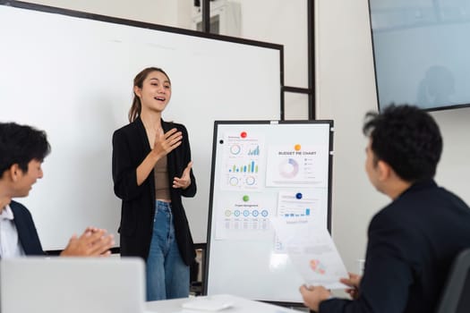 In a modern meeting room, a female professional passionately presents a detailed budget report, illustrating graphs and charts that capture the team's attention and encourage collaborative discussion.