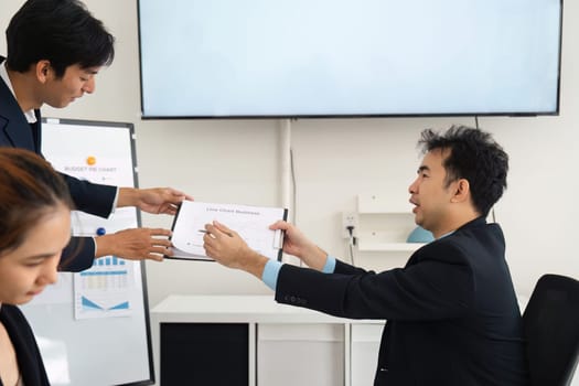 In a strategic meeting, one team member extends a report to a colleague, highlighting team collaboration and hands-on engagement in achieving shared business goals.