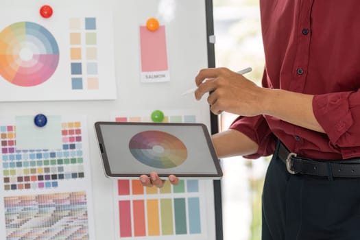 A creative professional reviews color schemes on a tablet, sharing insights with team members in a bright and modern workspace.
