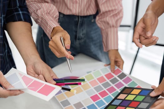 Team members enthusiastically discuss and choose color palettes from a variety of samples laid out on the table, blending ideas for their upcoming design.