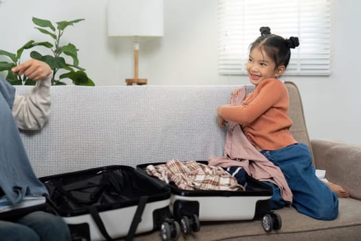 A cheerful girl helps her mom pack for their upcoming trip, showcasing teamwork and excitement as they share clothing choices.