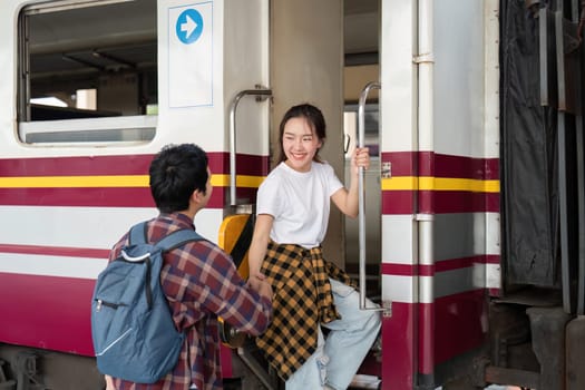 A couple prepares to board a train, with the woman smiling as she climbs aboard, excited for the travels that lie ahead together.