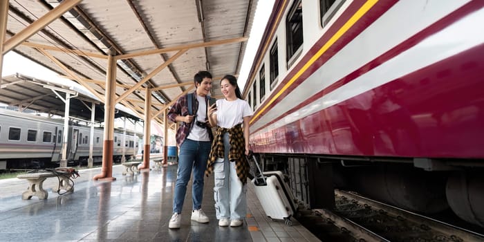 The couple stands side by side at the train station, laughing and enjoying a moment of connection as they await their train's arrival, showcasing a spirit of adventure.