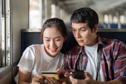 The couple shares a lighthearted moment on the train, using their devices and smiling at each other, representing modern travel companionship.