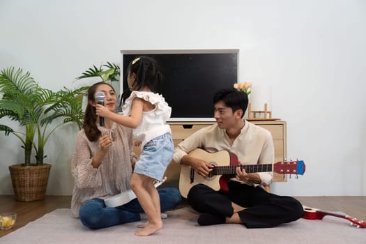 A lively scene as a little girl switches between a microphone and a ukulele, surrounded by her loving parents, radiating fun and creativity.