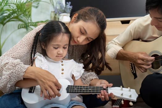 A nurturing moment as a mother guides her daughter in playing the ukulele, fostering creativity and love through family music time.