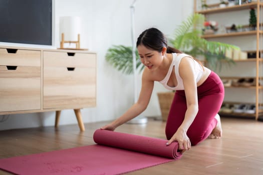 In a calm home environment, a woman rolls up her yoga mat after completing her practice, reflecting on her wellness journey and the benefits of her session.