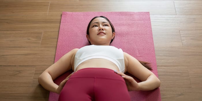 This image captures a woman in a reflective pose, engaging in relaxation techniques during her yoga practice at home.