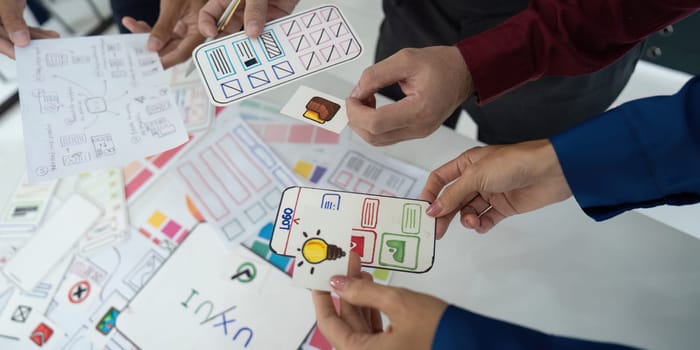 Three designers collaborate over a table filled with sketches and wireframes, refining concepts for a mobile app to enhance user experience and interface.