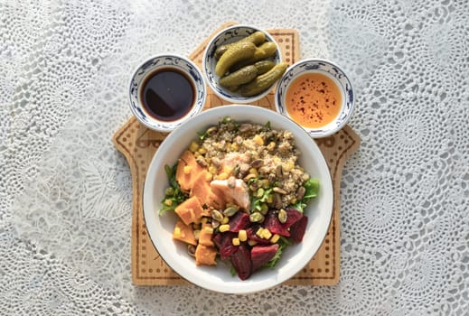Delicious Quinoa Salmon Poke bowl garnished with Leaves salad, Beetroot, Sweet potato, Sweet corn and Pistachio Served with Pickled Cornichons, Chilli oil and Balsamic vinegar. Top view, use it as your Wallpaper, Poster, Design and Copy space, Selected focus.
