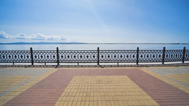 Metal railing bordering peaceful riverside, revealing serene waterscape beneath cloudless azure sky during sunny day