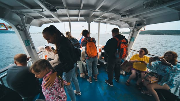 Backpacked travelers relaxing during ferry crossing, capturing scenic water journey under overcast sky and sharing travel moments