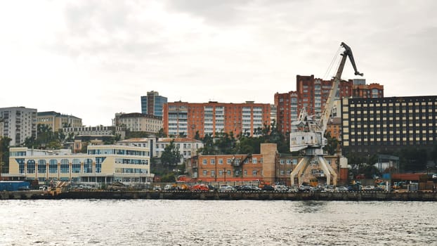 Industrial harbor scene showcasing a prominent cargo crane against the backdrop of vladivostok city skyline under a cloudy sky