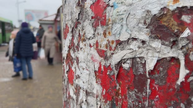 Close-up of a weathered red pole displaying tattered paper remnants, hinting at past advertisements, against a blurred urban backdrop