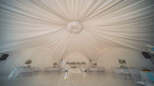 Elegant wedding venue decorated with flowing white fabrics and flower arrangements, creating a romantic atmosphere for celebrating marriage