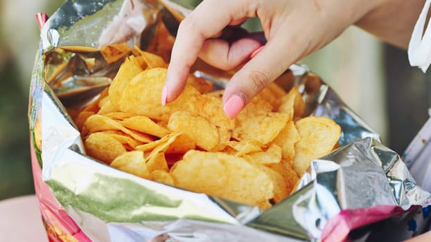 Woman reaching into crinkly chip bag, revealing compulsive snacking behavior and poor nutritional choices