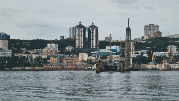 Industrial harbor cranes rising against vladivostok's skyline, heavy machinery silhouetted beneath overcast skies