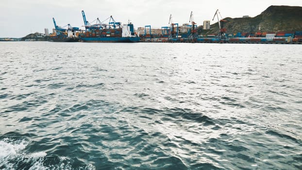 Cargo vessel navigating harbor with industrial cranes handling shipping containers under overcast sky, representing international maritime commerce