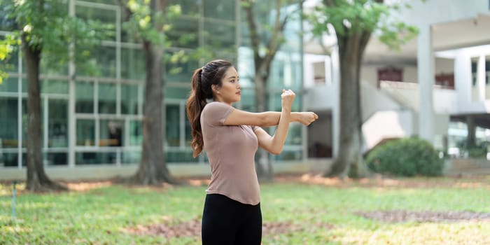 A young woman performs a stretching routine outside, focusing on her arm muscles to enhance flexibility and warm up her body in a refreshing environment.