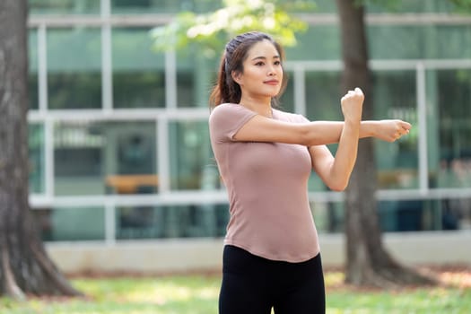 Focusing on her health, a woman performs an arm stretch in a serene park setting, promoting physical wellness and relaxation.