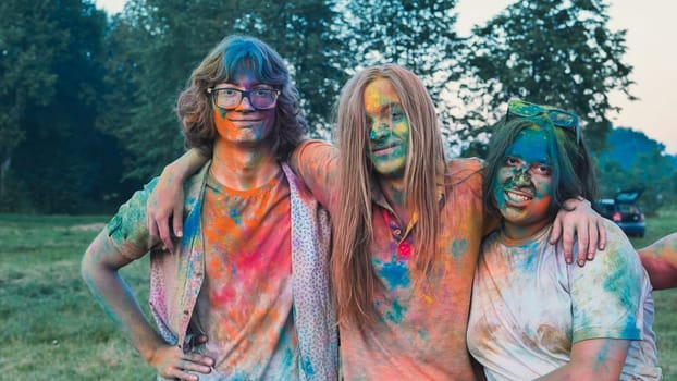 Three school friends are embracing each other, covered in vibrant holi powder, enjoying the colorful festivities