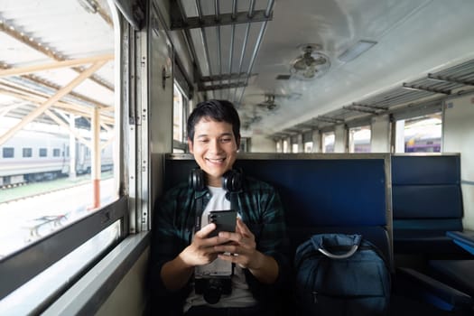 A smiling young man sits comfortably in a train, engaged with his phone while ready for his journey, embodying the excitement of travel and technology.