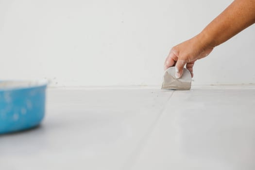 Worker holding a tool, applying and smoothing grout in tile gaps on a floor. A detailed image of professional tile installation and finishing.