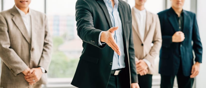Businessman in professional suit extends his open palm in gesture of request and handshake in an office setting. This portrays the concepts of trust cooperation and successful business relationships.
