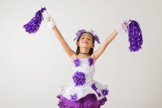 Adorable kid in cheerleading outfit with purple pom-poms. Studio photo on white, showcasing her happiness and energetic cheer. cheerleader kid