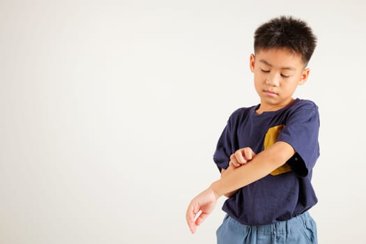 Asian little kid boy scratching itchy arm from a mosquito bite at studio shot isolated on white background, Portrait of Thai primary child dermatitis and scabies, Allergy symptoms, Malaria day concept