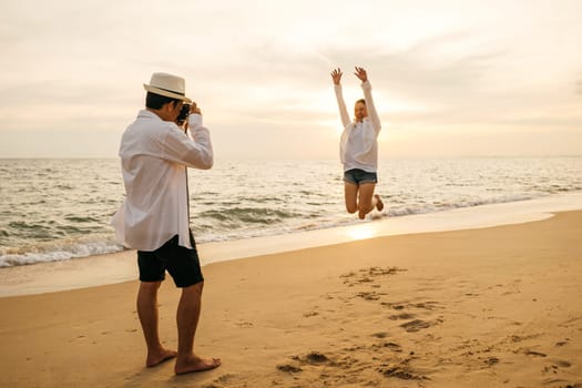 Love in focus as young couple dressed in white enjoys sunrise date on beach. boyfriend armed with camera lovingly captures snapshots of his girlfriend creating memories by ocean.