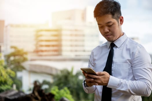 Young Asian businessman, software developer, smiles using phone app. Success in testing software outside office. Portrait of a satisfied CEO, standing, serious in technology