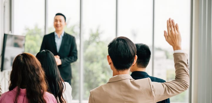 A group of professionals in a seminar meeting room raises their hands to ask questions, symbolizing an engaged audience ready to interact and learn. It's all about the concept of active participation.