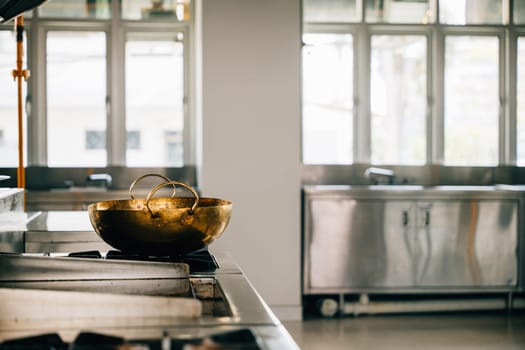 Within a modern restaurant's professional kitchen a shiny metal bowl is placed on the stove. Clean arrangement of chrome appliances equipment and new furniture. Working gas service is bright.