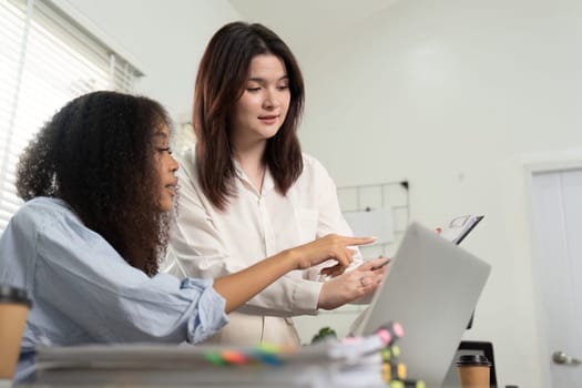 In a vibrant workspace, two women collaborate on solutions while reviewing information displayed on a laptop, emphasizing teamwork and innovation.