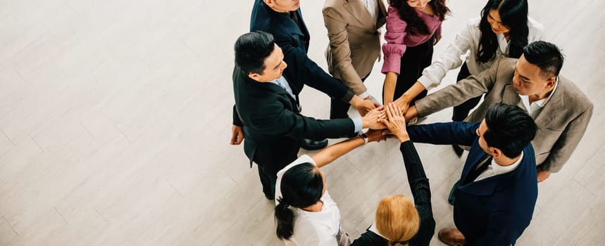 A top view captures four diverse businesspeople in a circle, hands stacked, symbolizing unity and teamwork. This image epitomizes success and global collaboration.