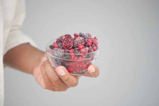 A person displays a bowl filled with assorted frozen berries.