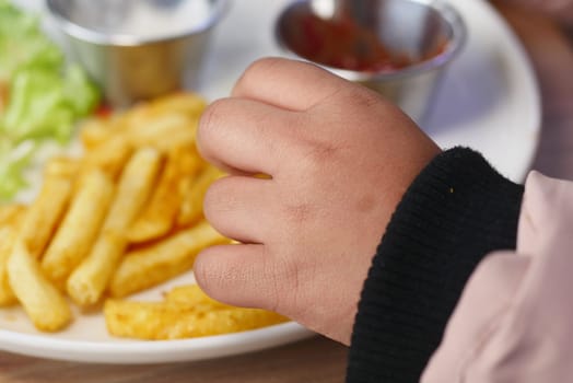 A small hand reaches for crispy fries beside lettuce and sauces.
