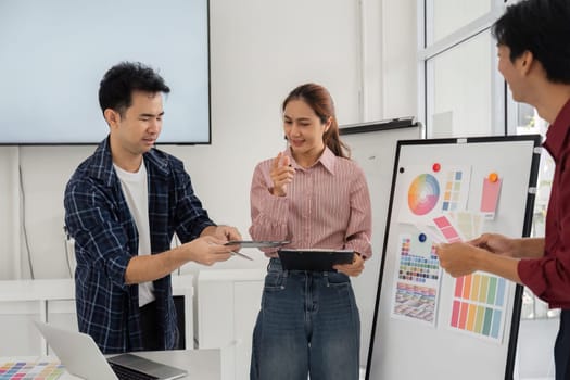 A group of creatives collaborates in a vibrant office, exchanging design ideas and feedback while examining color palettes on a tablet and board, fostering teamwork and innovation.