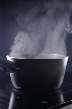 Steam rises from a pot placed on a reflective kitchen surface in low light.