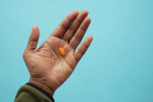 A hand with an orange tablet resting on the palm, set against blue.