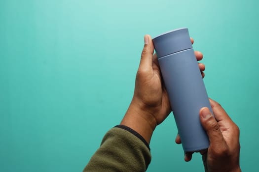Person grips a blue travel mug with both hands in a bright setting.
