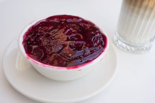 Fresh berry compote in a bowl beside a glass of creamy beverage.