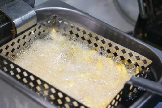 Golden fries bubbling in hot oil within a deep fryer basket.