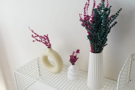 Colorful dried flowers arranged in stylish vases on a minimalist shelf.
